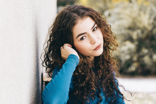 Woman with long brown curly hair wearing a blue top.